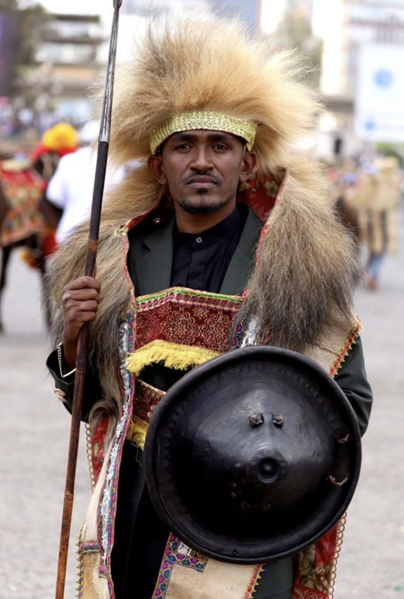 Musician Haacaaluu Hundeessaa poses in traditional clothing while holding a shield.